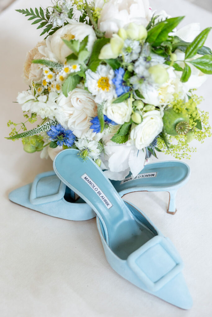 Blue bridal shoes in front of white, green, and blue bridal bouquet.